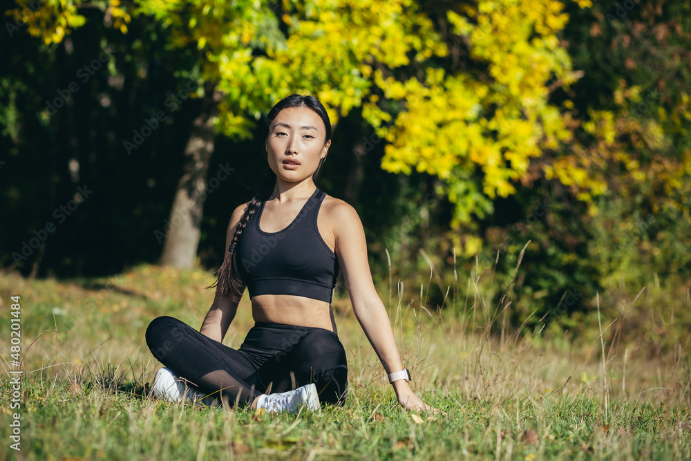 Beautiful Asian woman meditates in the woods on a sunny day, the athlete rests sitting in the lotus position and looks happily and calmly at the camera Beautiful Asian woman meditates in the woods on a sunny day, the athlete rests sitting in the lotus position and looks happily and calmly at the camera
