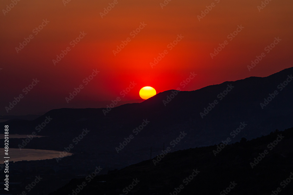 Orange sun on a red sky and mountains and sea are in the evening. Sunset