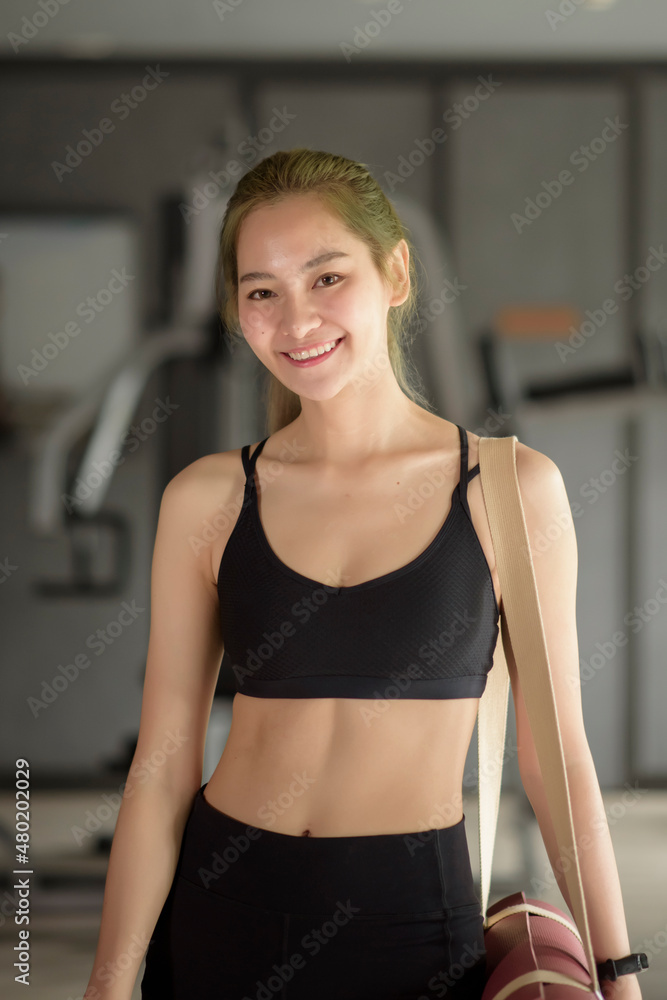Young beautiful Asian woman is standing in the gym , smiling after workout. Fitness and health concept