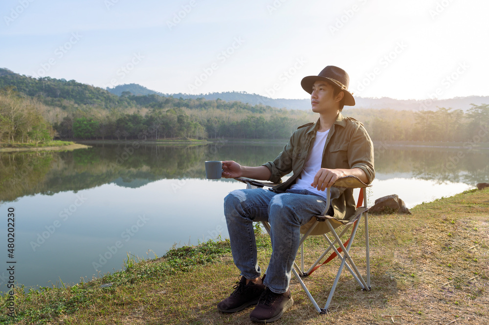Fototapeta premium Traveler man is drinking hot coffee over mountain and river view , concept of camping , nature tourism .
