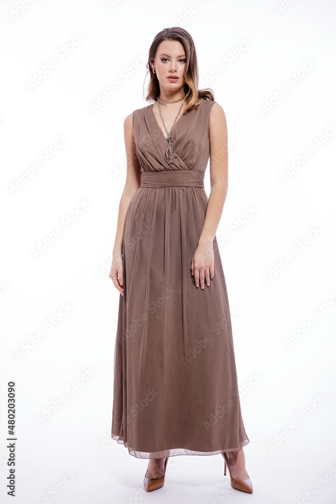 High fashion photo of beautiful elegant young woman in a pretty beige brown dress with a neckline, necklace posing on white background. Slim figure, make up, luxurious hair, shiny curls. Studio Shot High fashion photo of beautiful elegant young woman in a pretty beige brown dress with a neckline, necklace posing on white background. Slim figure, make up, luxurious hair, shiny curls. Studio Shot