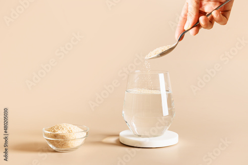 Tableau sur toile Woman adds psyllium fiber to glass of water on beige background