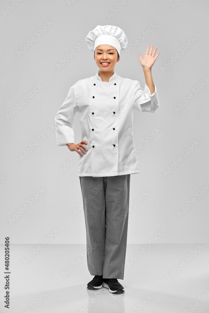 cooking, culinary and people concept - happy smiling female chef waving hand over grey background
