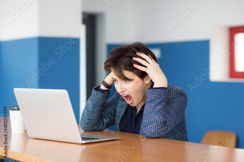 businesswoman sits at table with laptop, looks at notebook and gets upset. negative emotions, problem