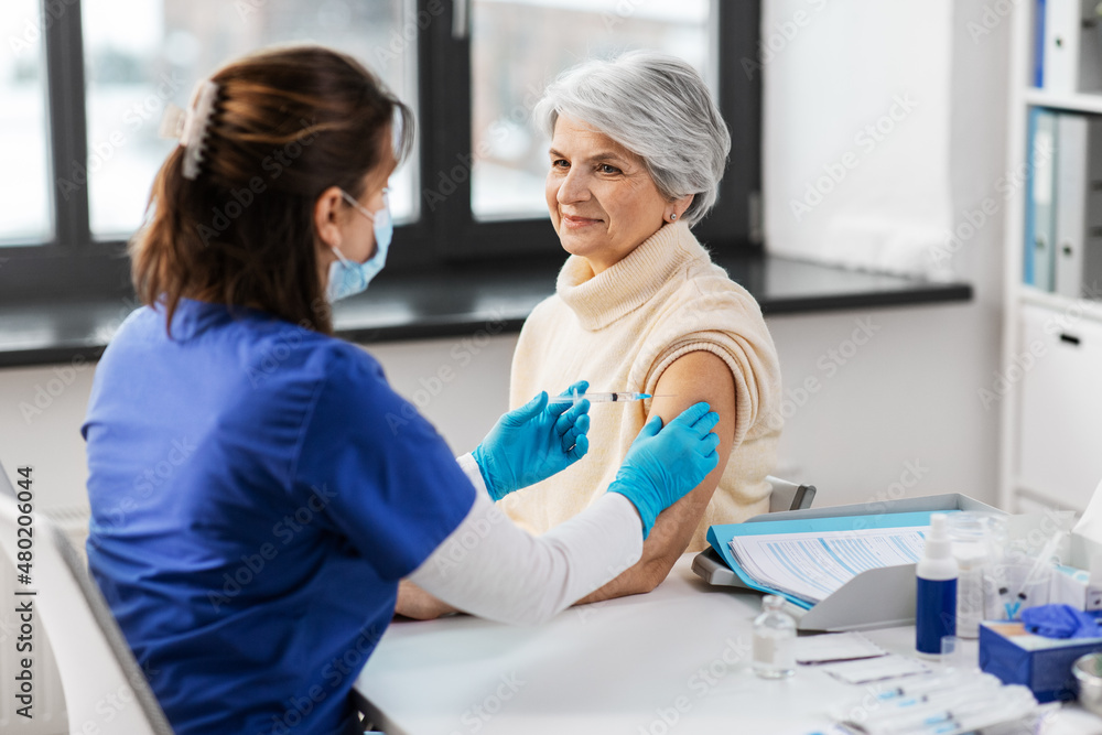 medicine, health and vaccination concept - doctor or nurse with syringe making vaccine or drug injection to senior woman at hospital medicine, health and vaccination concept - doctor or nurse with syringe making vaccine or drug injection to senior woman at hospital