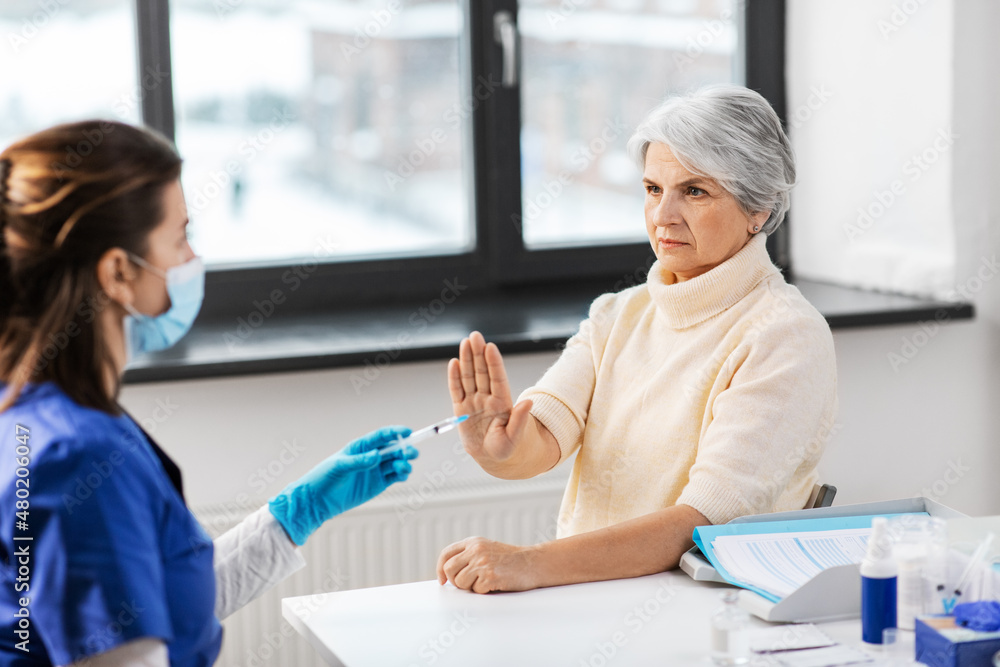 Obraz premium medicine, health and vaccination concept - doctor or nurse with syringe and senior woman refusing from vaccine or drug at hospital