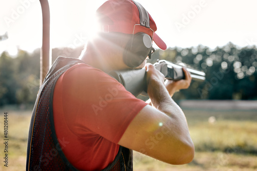 Rear view on handsome Male in cap and headset shooting at target on an outdoor shooting range at sunny day, training alone, confident and skilled, experienced. Shooting and Weapons. view from back.