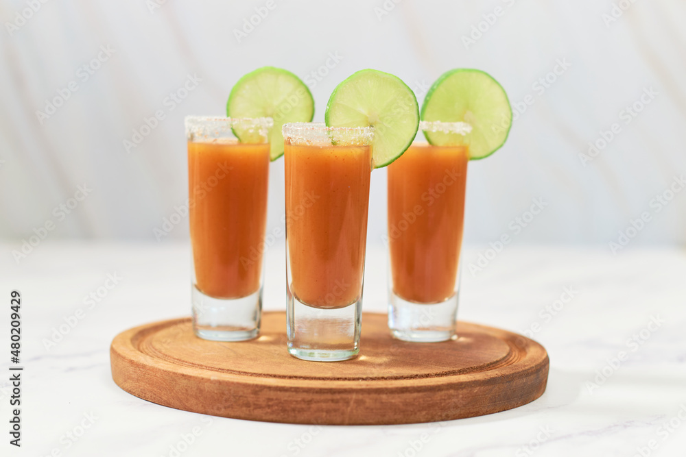 Fototapeta premium Three tequila shot with sangrita on wooden board. Mexican appetizer for tequila.