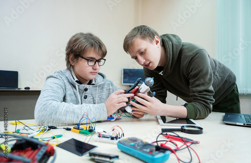 Teenager boy with instructor at robotics school makes robot managed from the constructor, child learns robot constructing.