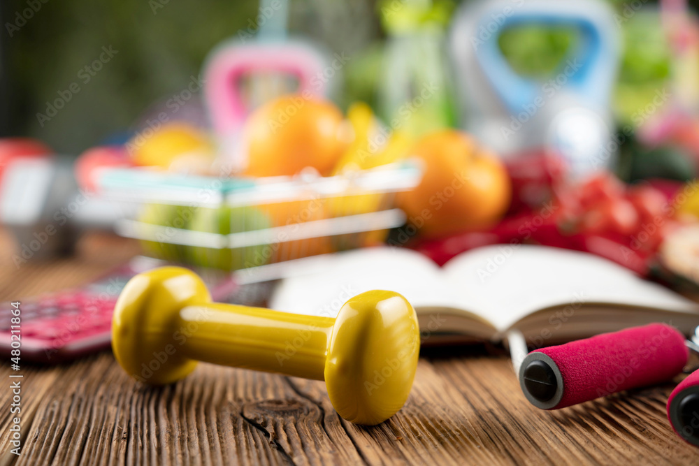 Fitness concept. Healthy nutrition: fruits and vegetables. Equipment for fitness exercises: weighing machine and dumbells on rustic wooden table.