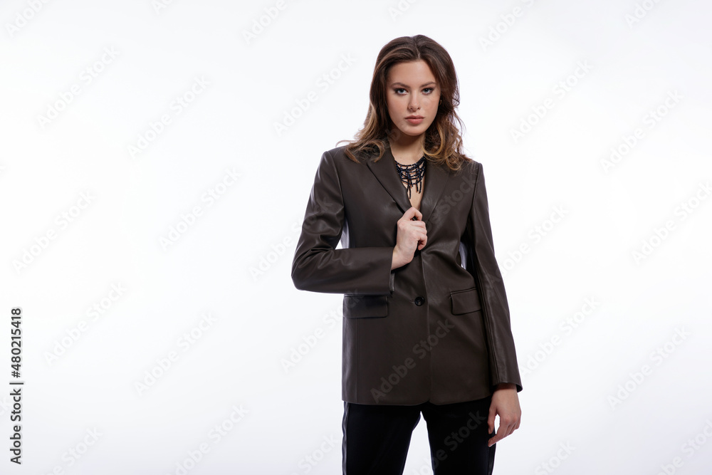 High fashion photo of beautiful elegant young woman in a pretty suit, leather dark olive khaki jacket, trousers, pants posing on white background. Studio shot. Slim figure, luxury hair, shiny curls High fashion photo of beautiful elegant young woman in a pretty suit, leather dark olive khaki jacket, trousers, pants posing on white background. Studio shot. Slim figure, luxury hair, shiny curls