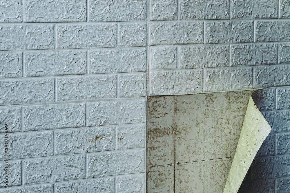 Obraz premium The wallpaper begins to peel off. Old white bricks wallpaper peeled off from the wall inside the room due to moisture or poor quality gluing. Repair and construction services concept. Selective Focus.