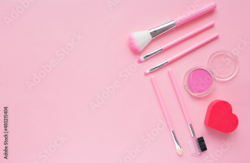 Cute pink makeup brushes, eye shadow and a heart shaped sponge. Cosmetics for a girl on valentine's day. Flat lay, top view, copy space