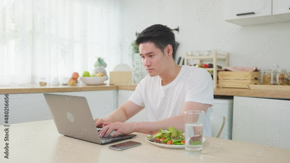 Asian business man eating healthy green salad while working from home. Asian business man eating healthy green salad while working from home.