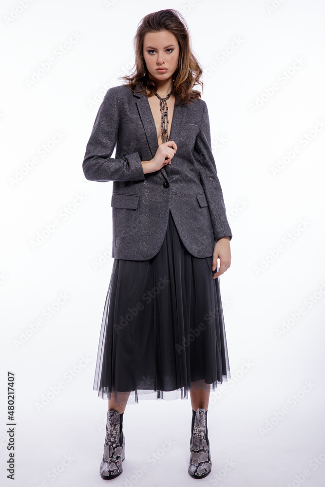 High fashion photo of beautiful elegant young woman in a pretty suit, gray sequined jacket, long skirt, snake skin boots, necklace posing on white background. Studio shot. Luxury hair, shiny curls High fashion photo of beautiful elegant young woman in a pretty suit, gray sequined jacket, long skirt, snake skin boots, necklace posing on white background. Studio shot. Luxury hair, shiny curls