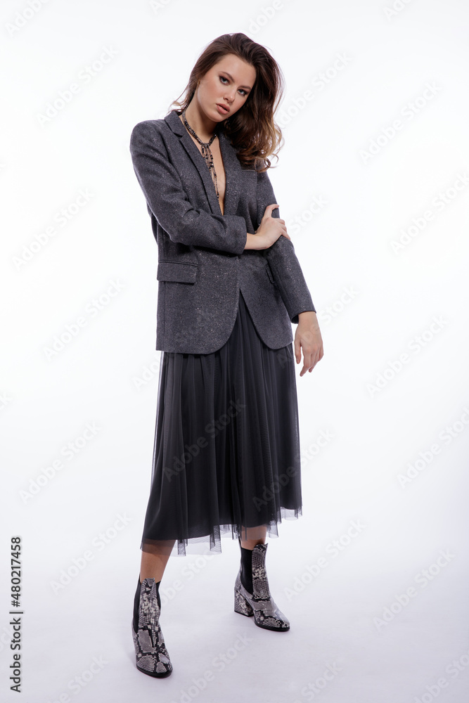 High fashion photo of beautiful elegant young woman in a pretty suit, gray sequined jacket, long skirt, snake skin boots, necklace posing on white background. Studio shot. Luxury hair, shiny curls High fashion photo of beautiful elegant young woman in a pretty suit, gray sequined jacket, long skirt, snake skin boots, necklace posing on white background. Studio shot. Luxury hair, shiny curls