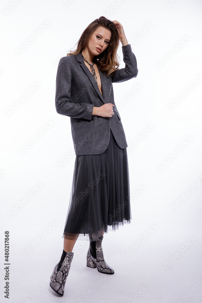 High fashion photo of beautiful elegant young woman in a pretty suit, gray sequined jacket, long skirt, snake skin boots, necklace posing on white background. Studio shot. Luxury hair, shiny curls High fashion photo of beautiful elegant young woman in a pretty suit, gray sequined jacket, long skirt, snake skin boots, necklace posing on white background. Studio shot. Luxury hair, shiny curls