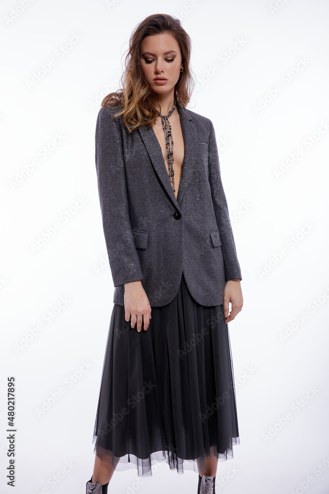 High fashion photo of beautiful elegant young woman in a pretty suit, gray sequined jacket, long skirt, snake skin boots, necklace posing on white background. Studio shot. Luxury hair, shiny curls High fashion photo of beautiful elegant young woman in a pretty suit, gray sequined jacket, long skirt, snake skin boots, necklace posing on white background. Studio shot. Luxury hair, shiny curls