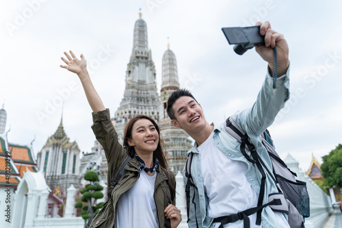 Asian couple backpacker use mobile phone selfie, take picture in city. 