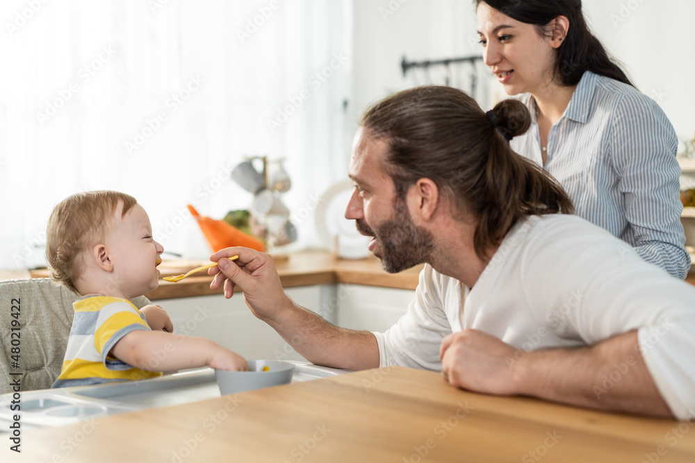 Caucasian beautiful parents take care of baby boy toddler in kitchen. Caucasian beautiful parents take care of baby boy toddler in kitchen.