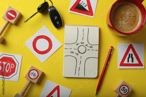 Flat lay composition with workbook for driving lessons and road signs on yellow background. Passing license exam photo