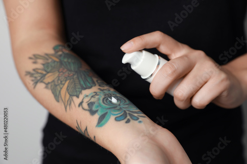 Woman applying cream on her arm with tattoos against light background, closeup © New Africa