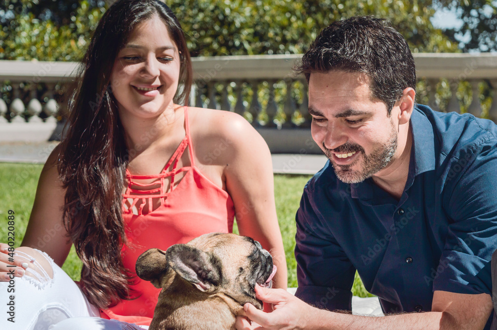 young bearded latino man playing with his french bulldog in the park with his girlfriend young bearded latino man playing with his french bulldog in the park with his girlfriend