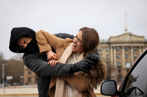 Woman defending herself from attacker near car outdoors photo