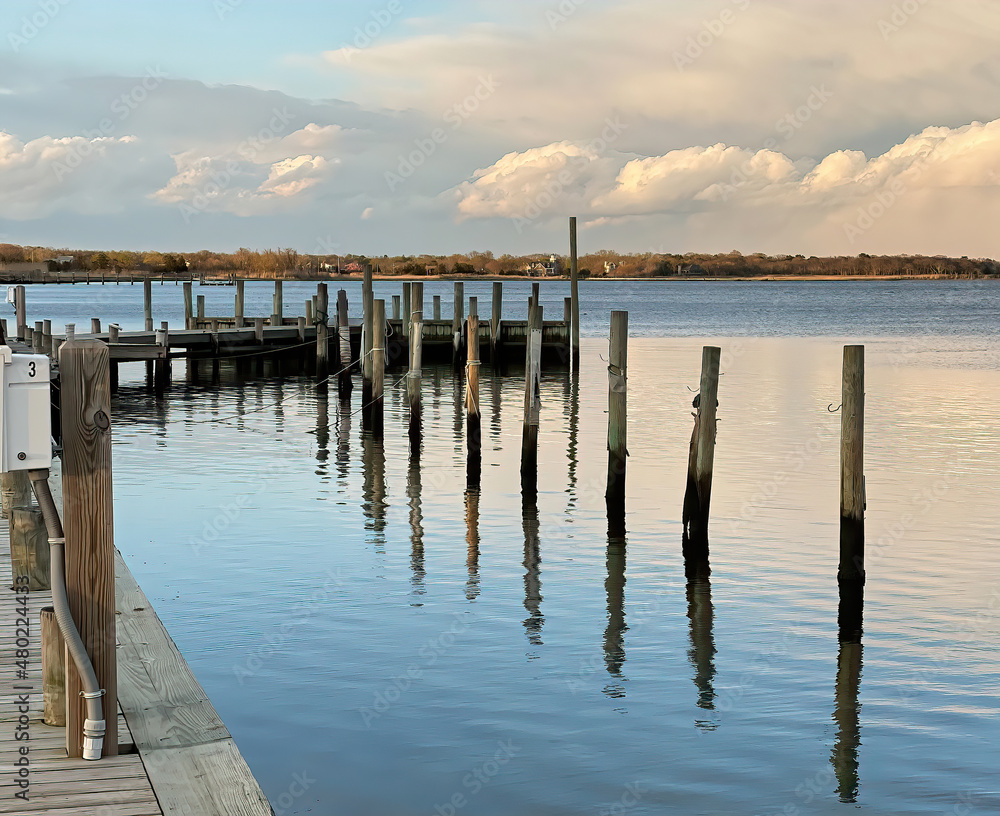 Empty bayside boat dock on calm water with soft, dramatic sky