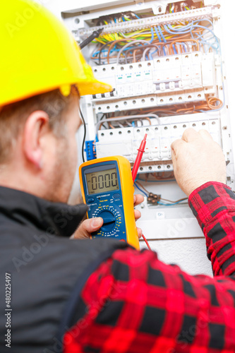 The electrician measures the electric current on the wires and the fuse switch. Multimeter in the hand of electricians detail.