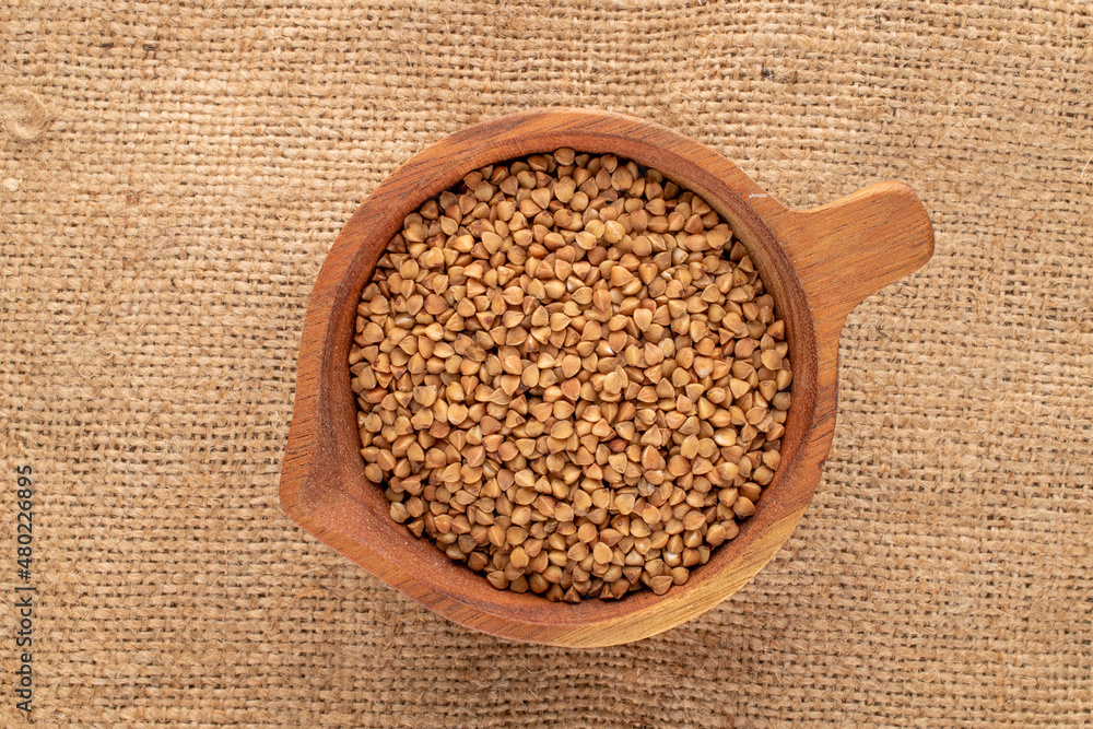 Raw organic buckwheat with a wooden cup on burlap, macro, top view. Raw organic buckwheat with a wooden cup on burlap, macro, top view.
