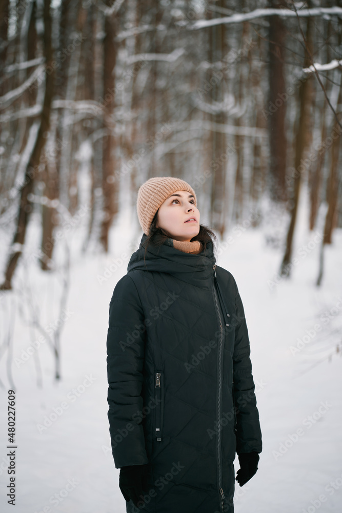 Beatiful woman looks up in the winter forest. Single girl wearing winter hat and scarf. Beatiful woman looks up in the winter forest. Single girl wearing winter hat and scarf.
