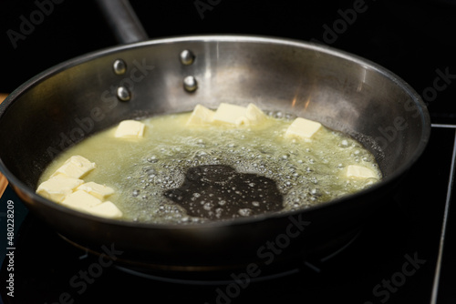 Pieceses of butter melted in a frying pan on a gas stove