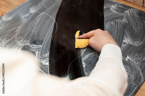A young woman is cleaning an induction electric hob. Cleaning in the kitchen. Electric oven cleaning. Cleaning company concept.