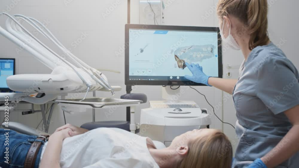 Girl doctor dentist demonstrates a 3D model of teeth on a touch monitor, rotates her hands. Dental consultation in the clinic, diagnostics. Jaw scan, digital imprint, medical digital technology. Girl doctor dentist demonstrates a 3D model of teeth on a touch monitor, rotates her hands. Dental consultation in the clinic, diagnostics. Jaw scan, digital imprint, medical digital technology.