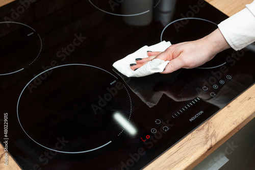 A young woman is cleaning an induction electric hob. Cleaning in the kitchen. Electric oven cleaning. Cleaning company concept.