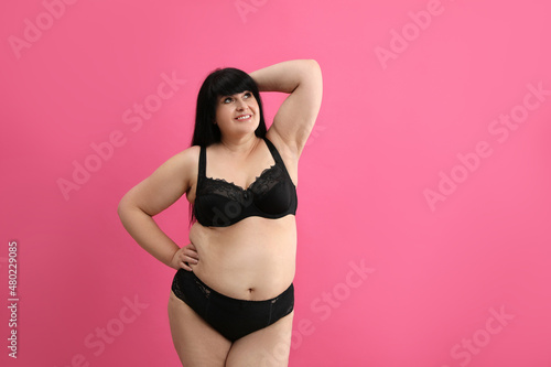 Beautiful overweight woman in black underwear on pink background, space for text. Plus-size model