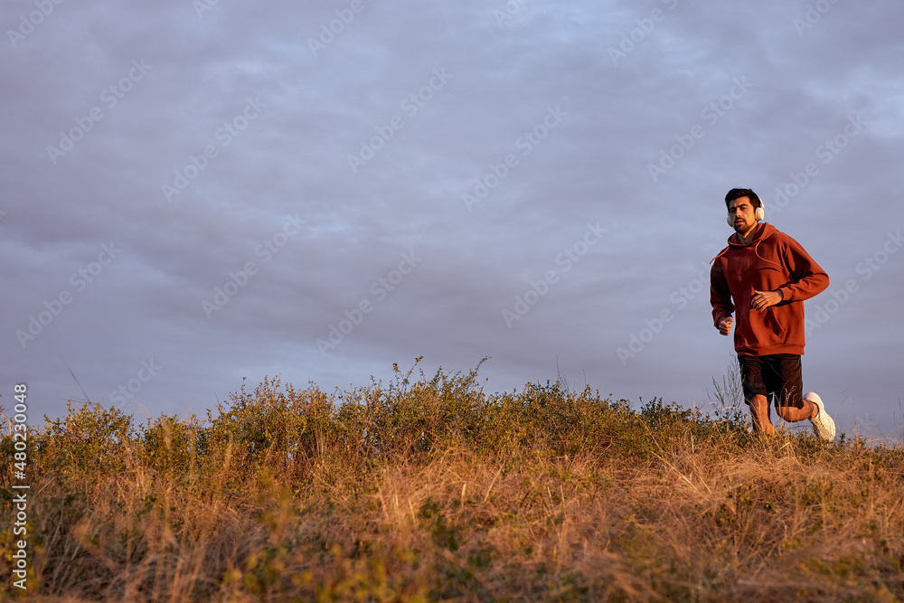sunset and running athletic man on field. Healthy lifestyle concept. caucasian fitness male in sprotive outfit jogging alone, at sunset or sunrise in field in nature, wonderful landscape. sunset and running athletic man on field. Healthy lifestyle concept. caucasian fitness male in sprotive outfit jogging alone, at sunset or sunrise in field in nature, wonderful landscape.