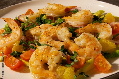 Bright salad in a white plate on the loft table with shrimp, red tomatoes and herbs.
