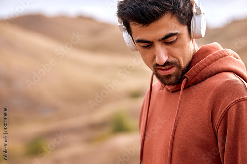 calm caucasian male with big earphones headphones listen to music relaxed after workout jogging  running  leading healthy lifestyle  keeping fit. man in red hoodie take a break  looking down