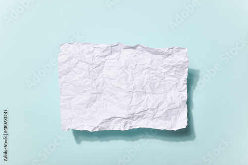 A crumpled piece of paper with a shadow and an empty space on a light blue background. © Irina Lesovaia