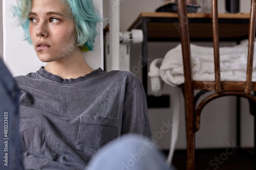 Unhappy sad worried young woman in casual wear sit on bedroom floor alone troubled with loneliness, upset about solitude mental problem look at window think of bad mistake, biting lips photo