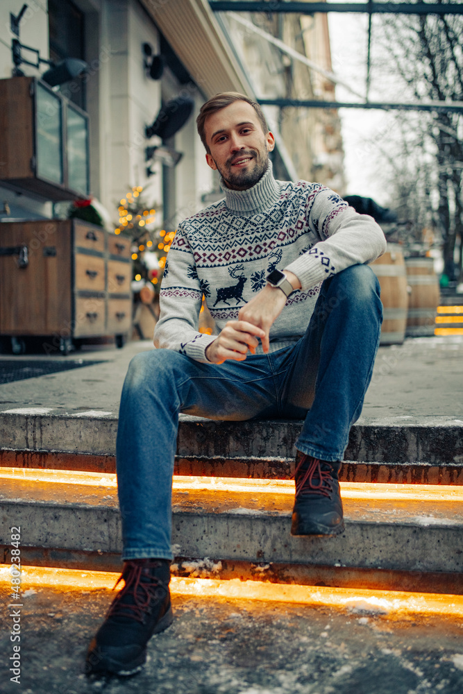 Man sits on stairs in street decorated for Christmas.