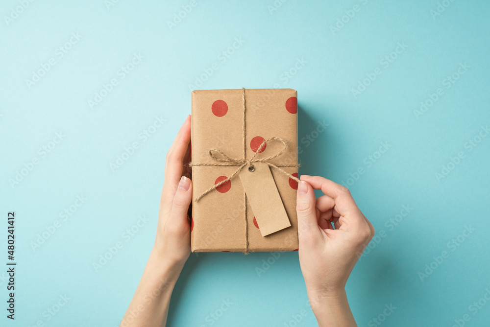 First person top view photo of valentine's day decorations female hands untying twine bow on craft paper giftbox with polka dot pattern and tag on isolated pastel blue background with copyspace First person top view photo of valentine's day decorations female hands untying twine bow on craft paper giftbox with polka dot pattern and tag on isolated pastel blue background with copyspace