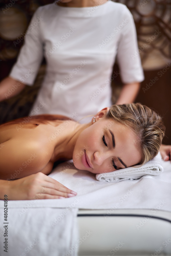 attractive young caucasian woman is getting chocolate massage at spa. Client's eyes are closed with relaxation. professional masseuse is applying substance on female back with brush, close-up. attractive young caucasian woman is getting chocolate massage at spa. Client's eyes are closed with relaxation. professional masseuse is applying substance on female back with brush, close-up.