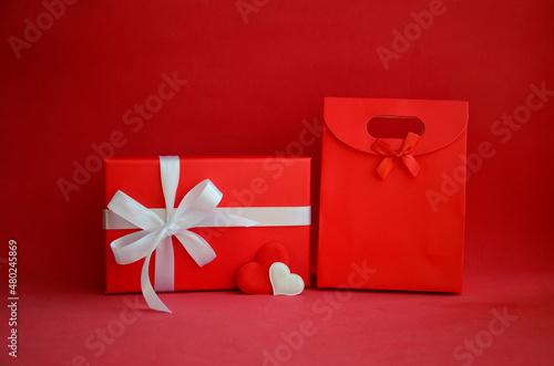 Red gift box with white bow, shopping bag and hearts on red background with copy space. Gift for Valentine's Day, March 8, mother's day, birthday.