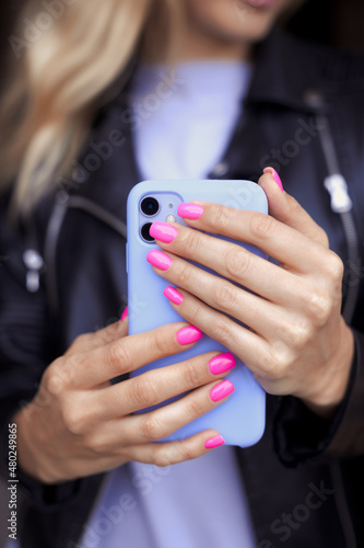 Vertical photo of female hands with bright neon pink manicure hold a smartphone in a purple case. No face. Young girl with fashion violet manicure taking a selfie photo on a mobile phone