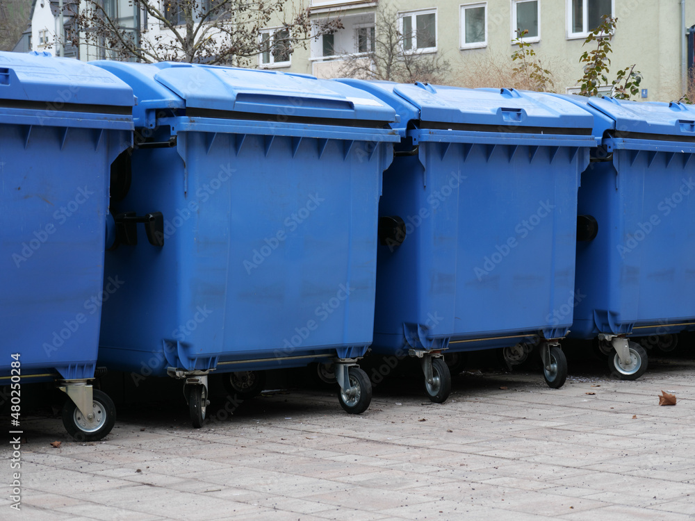 Eine Reihe von blauen Müllcontainern für Papiermüll in einem Hof Eine Reihe von blauen Müllcontainern für Papiermüll in einem Hof