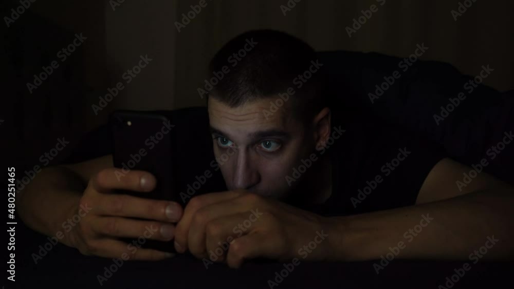 a young guy looks at the phone before going to bed at night and falls asleep. Examines information on the phone a young guy looks at the phone before going to bed at night and falls asleep. Examines information on the phone