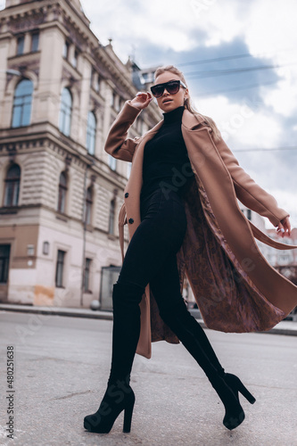 Young beautiful girl in a beige coat and sunglasses walks through the city